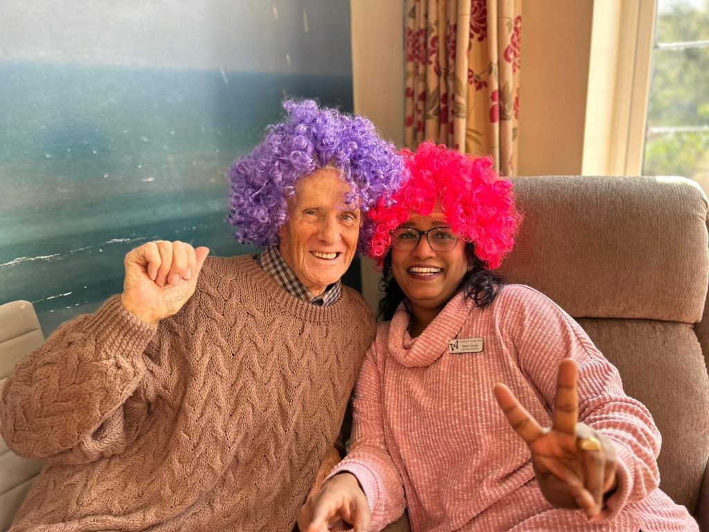 A resident smiling with the home manager in funny wigs